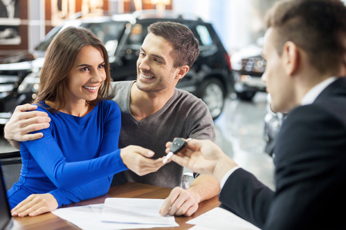 Now her dream comes true. Car salesman giving the key of the new car to the young attractive owners