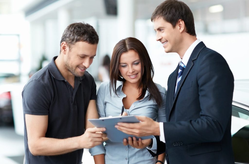 People looking at a clipboard in a car dealership