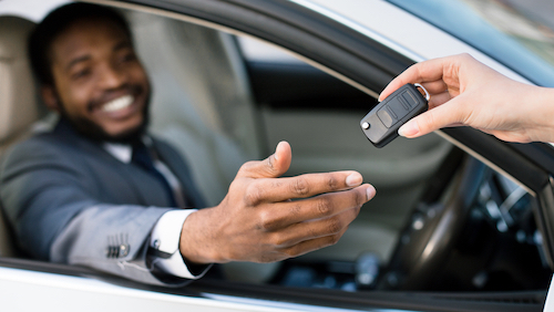 Car salesman giving keys to happy man, sitting in white auto in dealership showroom